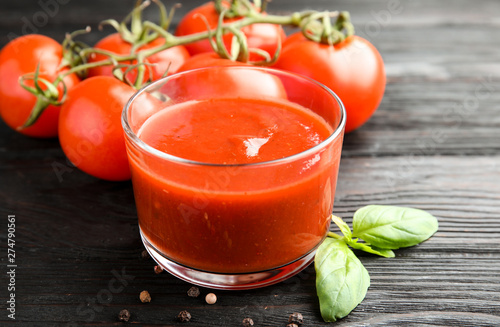 Glass of tomato sauce with basil on wooden table, closeup