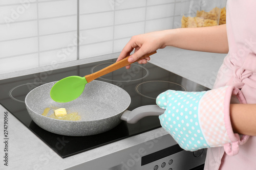 Woman stirring butter in frying pan on electric stove, closeup photo