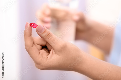 Woman holding pill and glass of water on blurred background  closeup. Space for text
