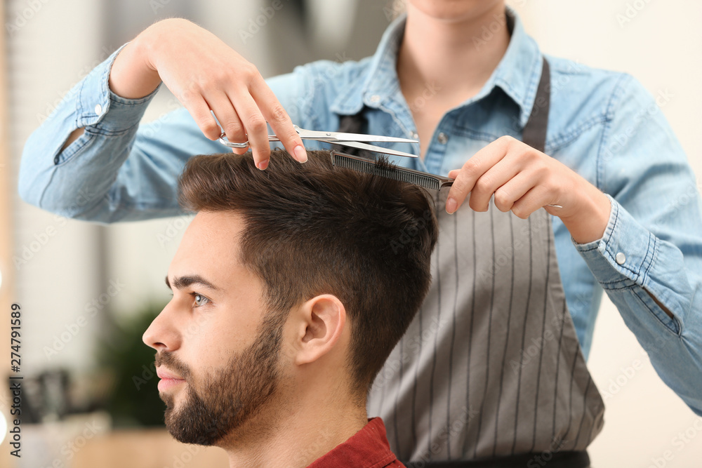 Fototapeta premium Barber making stylish haircut with professional scissors in beauty salon