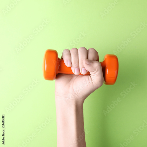 Woman holding vinyl dumbbell on color background, closeup