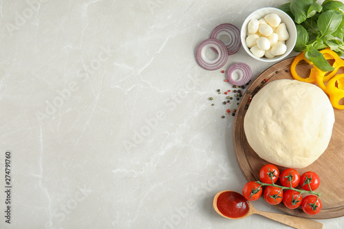 Flat lay composition with dough and ingredients for pizza on marble table, space for text