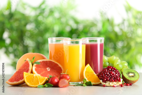 Three glasses with different juices and fresh fruits on table against blurred background