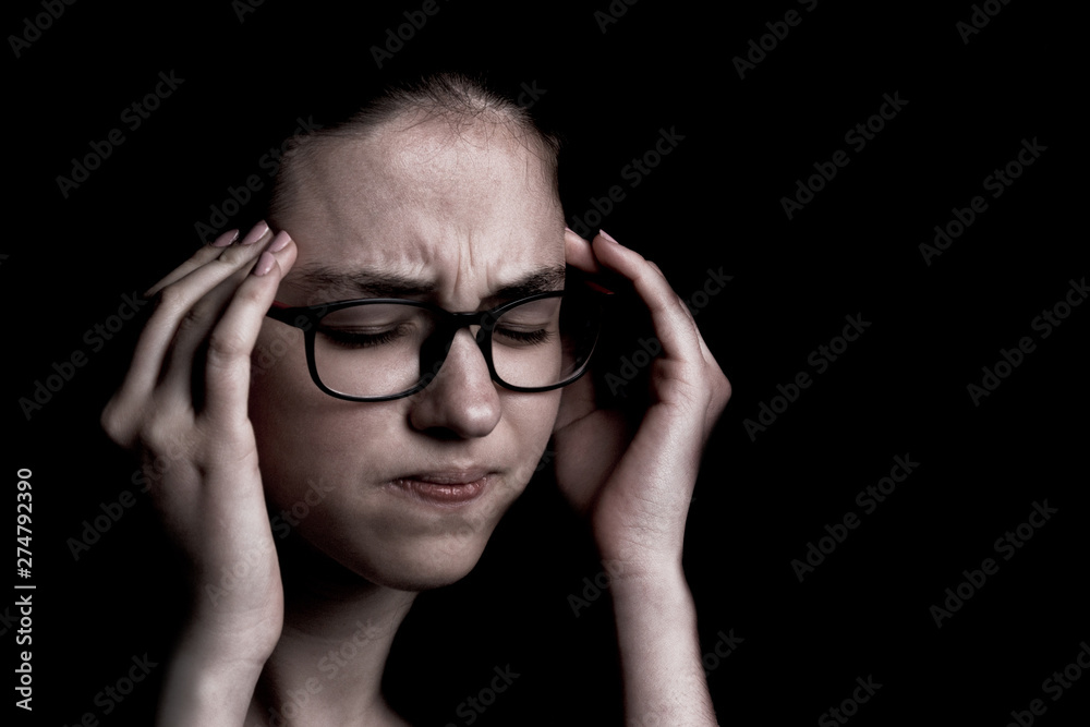 the severe headache, the teenager, the girl keeps hands on the head on the black background the severe headache, the teenager, the girl keeps hands on the head on the black background