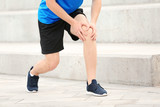 Man in sportswear suffering from knee pain on stairs, closeup