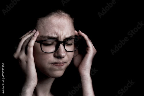 the severe headache, the teenager, the girl keeps hands on the head on the black background