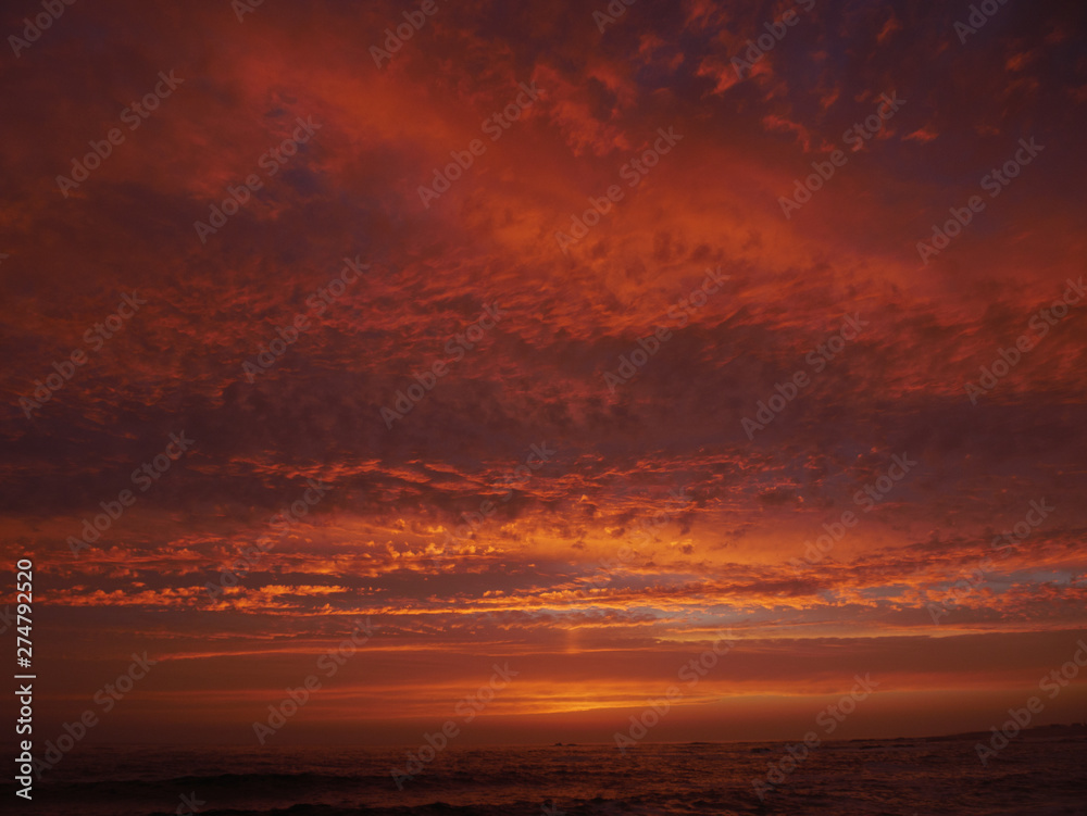 Vivid red sky at sunset on beach with dramatic clouds and dark sea