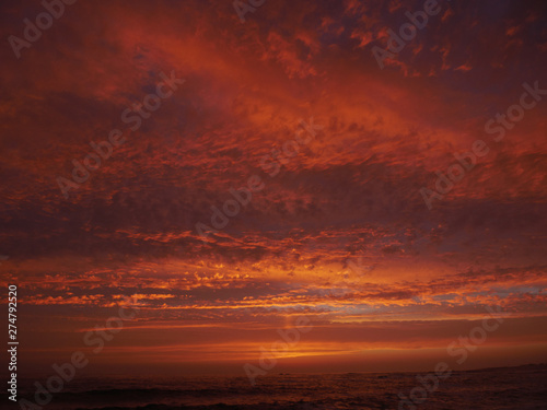 Vivid red sky at sunset on beach with dramatic clouds and dark sea
