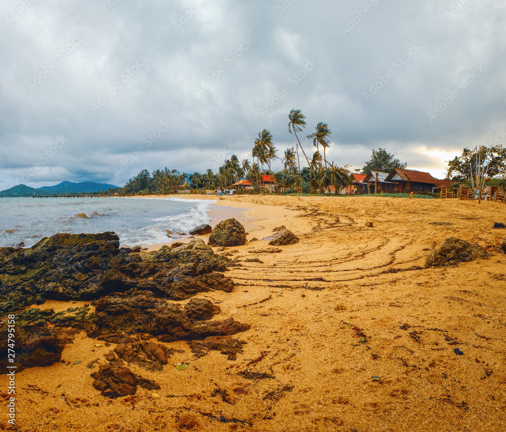 Obraz premium Cloudy evening view of Maenam beach, Koh Samui, Thailand. Beautiful seascape with sea waves and rocks scattered on beach sand. Rainy ominous grey storm clouds - dramatic sky.