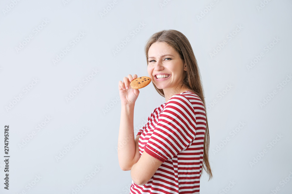Beautiful young woman with tasty cookie on light background Beautiful young woman with tasty cookie on light background