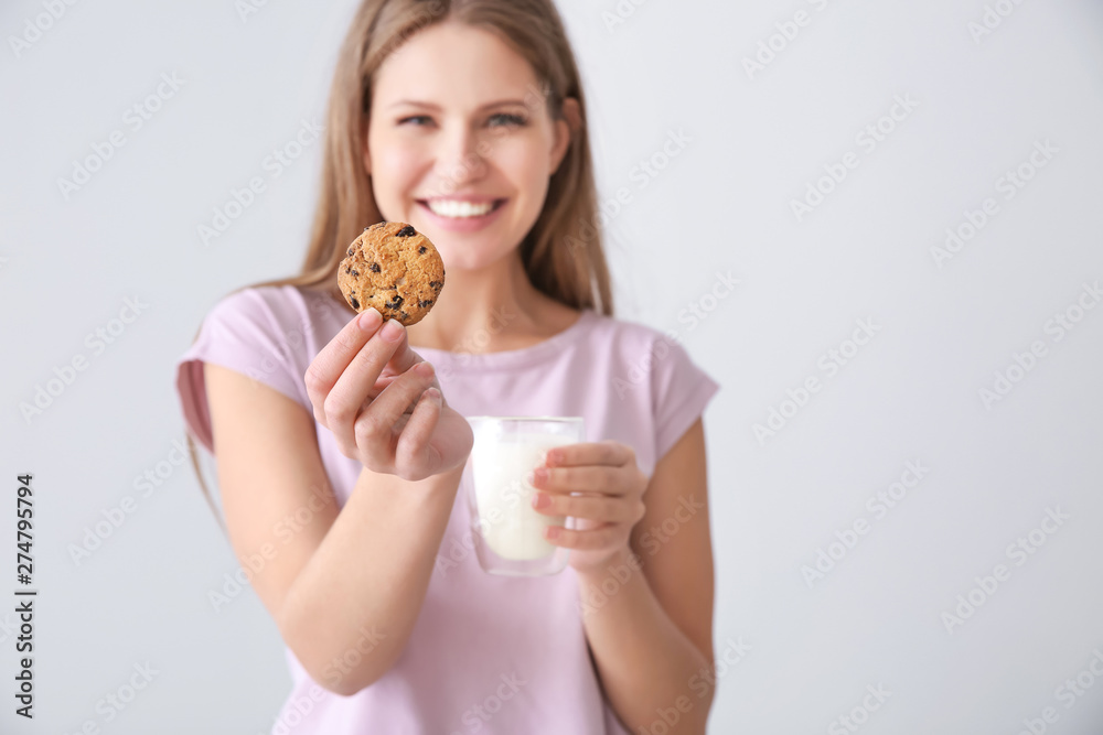 Beautiful young woman with tasty cookie and glass of milk on light background Beautiful young woman with tasty cookie and glass of milk on light background