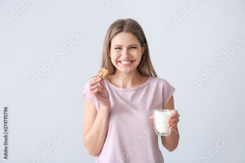 Beautiful young woman with tasty cookie and glass of milk on light background
