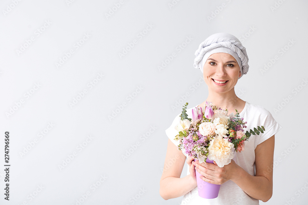 Woman after chemotherapy with bouquet of flowers on light background