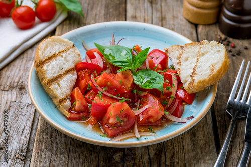 Tomato salad with red onion and bread on wooden table