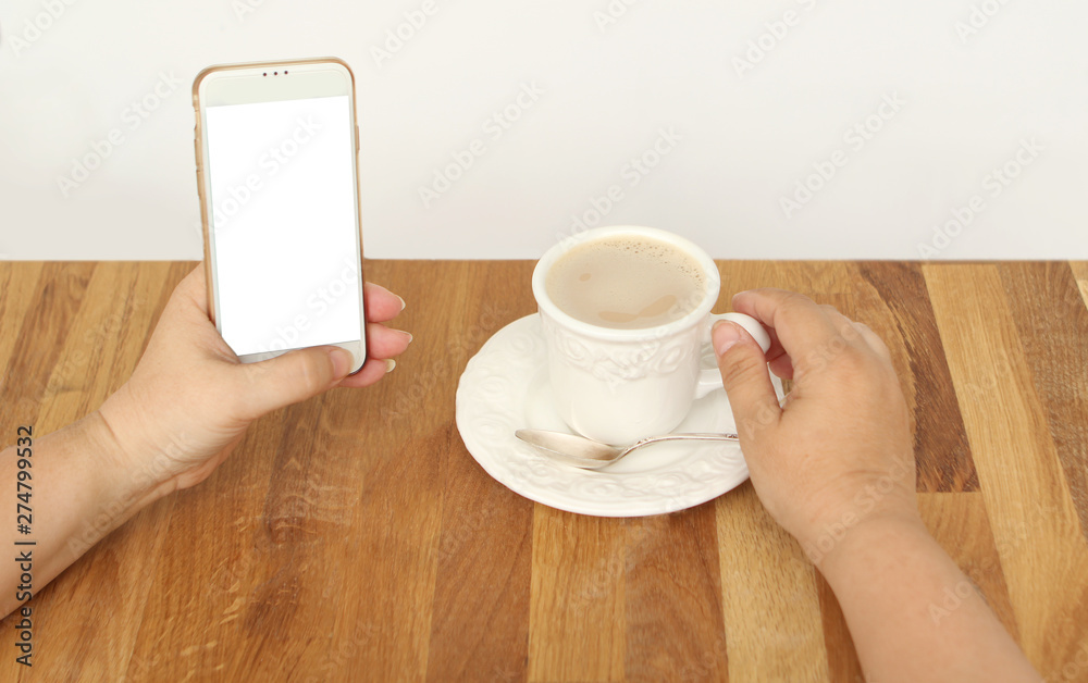 Mock up image of female hands holding white mobile phone with empty white screen and cup of coffee