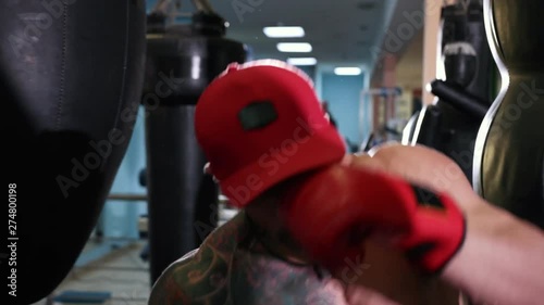 Handsome young man with a bare torso in a red cap and boxing gloves boxing on goal. Wide angle, Prores, Slow Motion photo