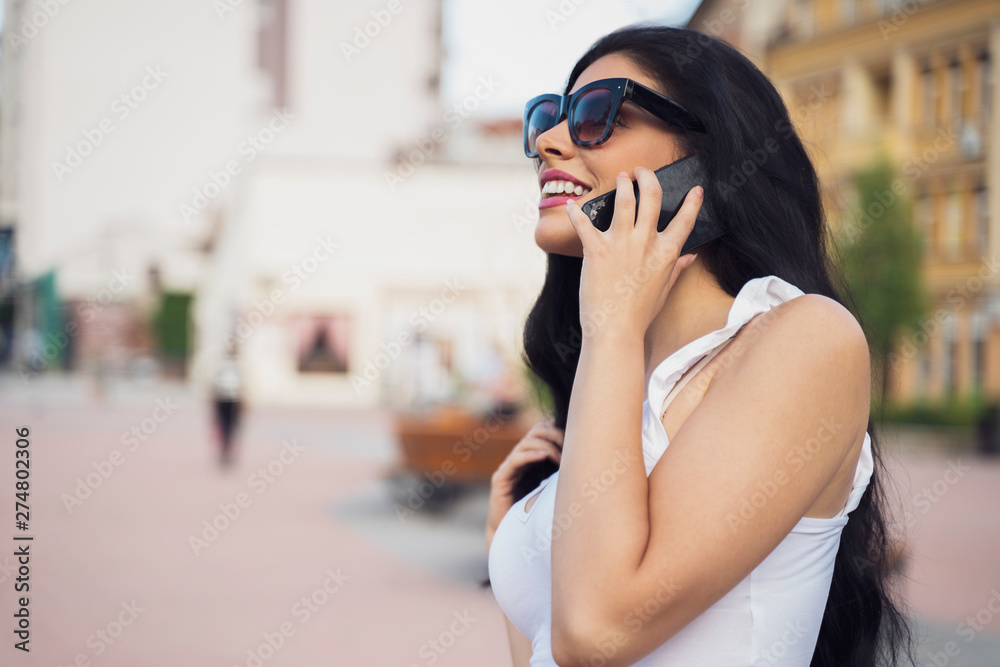 Obraz premium Gorgeous young woman with sunglasses talking on smartphone outdoors , blurred background 
