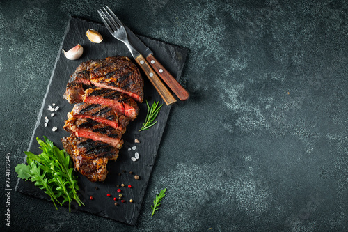 Sliced steak ribeye, grilled with pepper, garlic, salt and thyme served on a slate cutting Board on a dark stone background. Top view with copy space. Flat lay