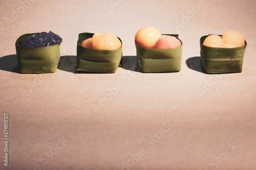 Thai sweets in banana leaves that are arranged in rows. Purple rose steamed layer cake, golden jackfruit seeds, thai mung bean marzipan and golden drops.