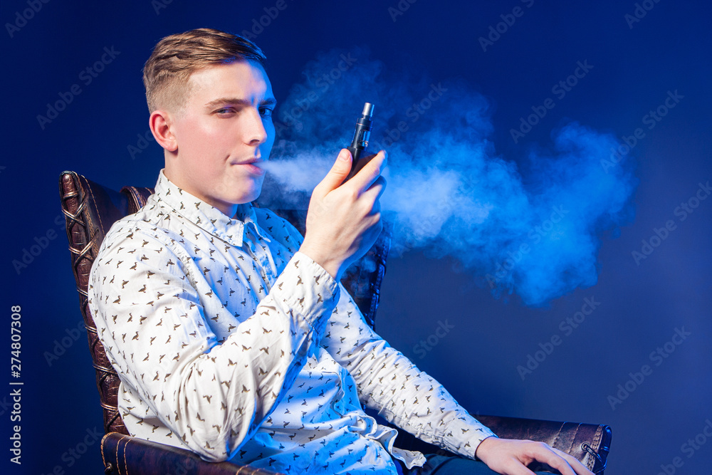 Vaping. Young man with a vape. A man blows smoke. A person smokes an electronic  cigarette. The man looks intriguingly. The piercing male gaze. Beau. Dandy.  Smoke break. Stock Photo | Adobe
