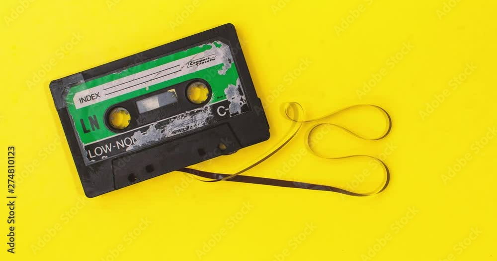 old retro cassette tape with grunge label rewinding pulled tape on yellow background stop motion