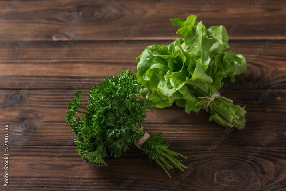 A bunch of parsley and a bunch of lettuce on a brown wooden table. A bunch of parsley and a bunch of lettuce on a brown wooden table.