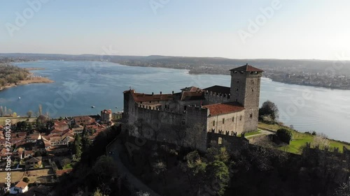 A mavic air drone is moving up behind the Rocca Di Angera revealing the beautiful lake landscape in a perfect sunny day