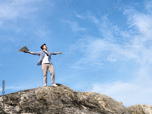 Asian tourist standing on the rock and raising hands with blue sky background,