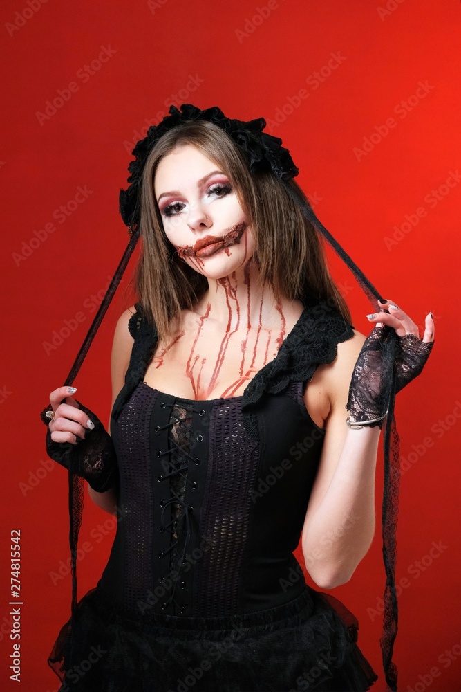 Halloween party outfit. Makeup and black clothes for All Saints Day. Beautiful girl in a scary image on a red background. Halloween party outfit. Makeup and black clothes for All Saints Day. Beautiful girl in a scary image on a red background.