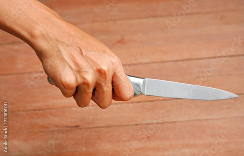 Hand holding knife against plank wood