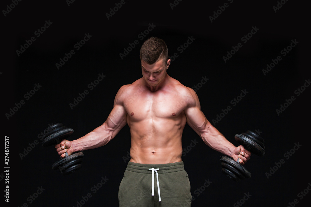 Handsome power athletic man with dumbbell confidently looking forward. Strong bodybuilder with six pack, perfect abs, shoulders, biceps, triceps and chest. Strong Athletic Man - Fitness Model showing