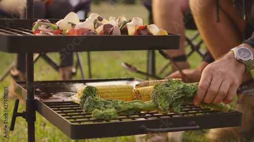 Placing broccolini vegetables on an open campfire BBQ to cook alongside some corn cobs and lamb kebab skewers photo