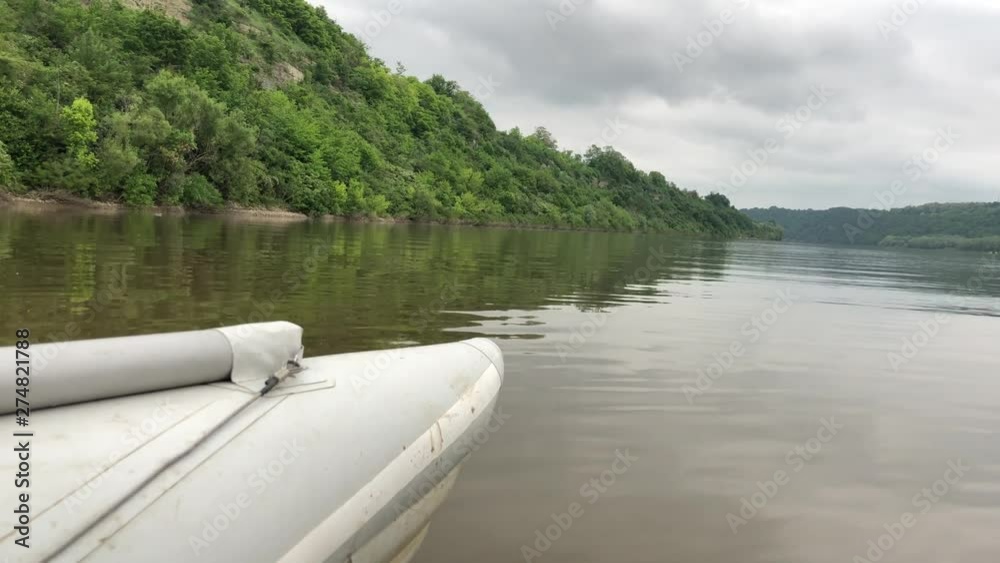 Rafting on a catamaran on the calm river Dniester. The front of the boat can be seen in the frame. Green coast reflected from the water. Rafting on a catamaran on the calm river Dniester. The front of the boat can be seen in the frame. Green coast reflected from the water.