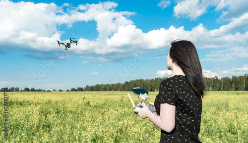The girl controls the quadcopter. Drone in flight over the field. The operator of the drone. Forest, sky and clouds.