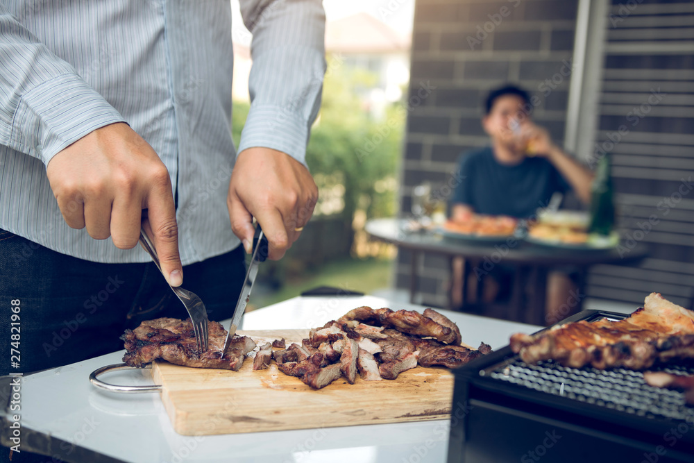 Asian friends are using a knife and a fork to cut the grilled meat on the chopping board to bring food together with friends celebrate with fun.