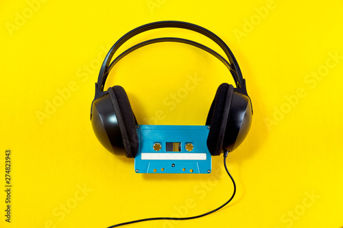 Top view of Headphone and blue classic tape cassette against yellow isolated background. Listening music theme.