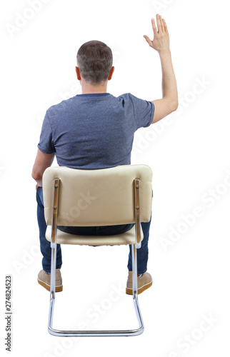 Back view of a man sitting on a chair and raising a hand to ask a question.