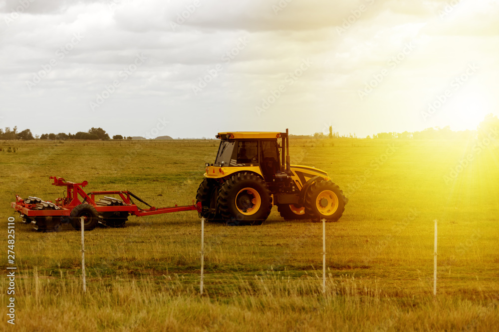 Fototapeta premium Tractor drags a grinder during sunset on a farm