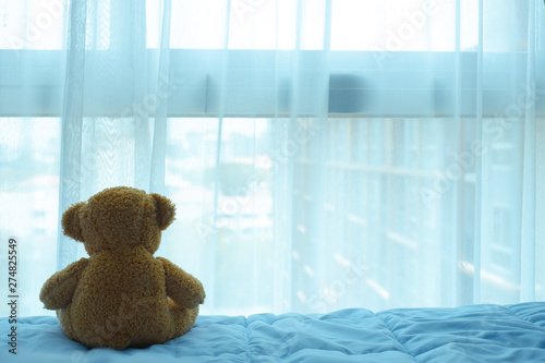brown bear doll sitting on the bed and looking thru the curtain and window