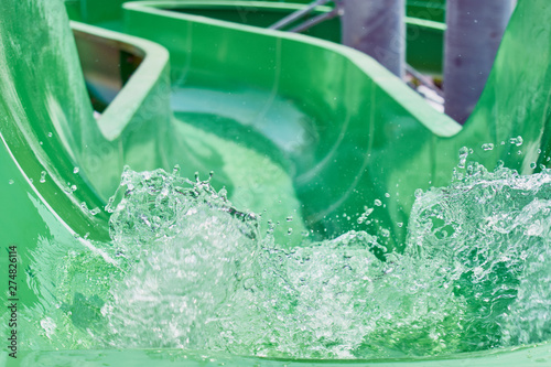 The stream of splashing water on green hill in water park for riding children.