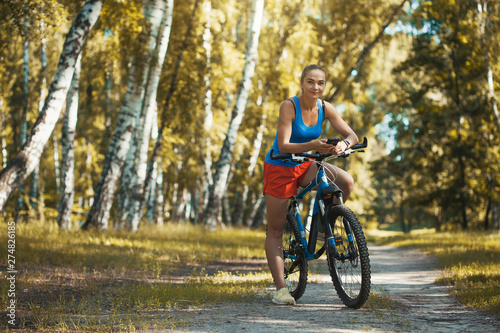cute blonde woman cyclist cycling mountain bike on the birch forest trail