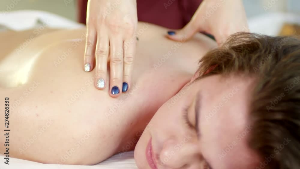 Tilt up of young Caucasian man lying on massage table with closed eyes and receiving relaxing shoulders massage Tilt up of young Caucasian man lying on massage table with closed eyes and receiving relaxing shoulders massage