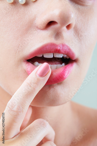 Close-up image of young woman touching her full sensual pink lips with finger