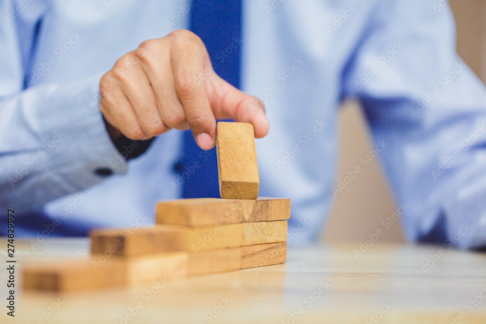 Hand of businessman pulling out or placing wood block on the tower, plan and strategy in business. Hand of businessman pulling out or placing wood block on the tower, plan and strategy in business.