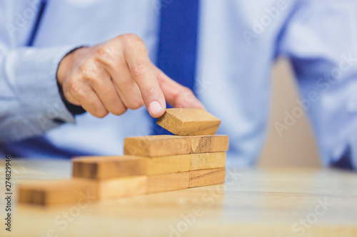 Hand of businessman pulling out or placing wood block on the tower, plan and strategy in business. © A Stockphoto