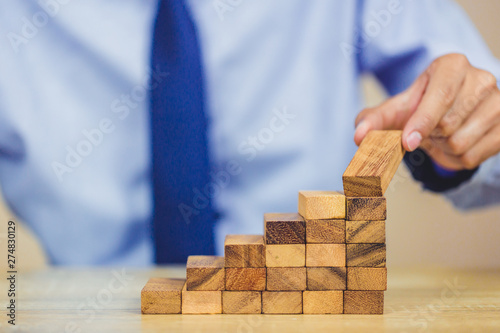 Hand of businessman pulling out or placing wood block on the tower, plan and strategy in business.