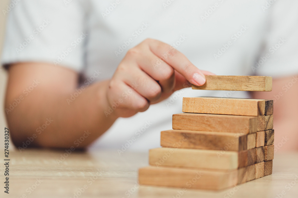 Hand of businessman pulling out or placing wood block on the tower, plan and strategy in business. Hand of businessman pulling out or placing wood block on the tower, plan and strategy in business.