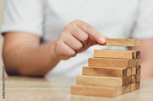 Hand of businessman pulling out or placing wood block on the tower, plan and strategy in business.