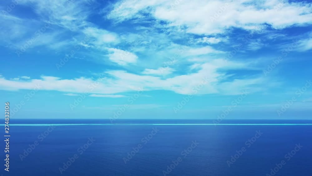 A blue summer sky with clouds above the deep blue Philippine Sea. Pan left, wide angle. One third of water. A blue summer sky with clouds above the deep blue Philippine Sea. Pan left, wide angle. One third of water.