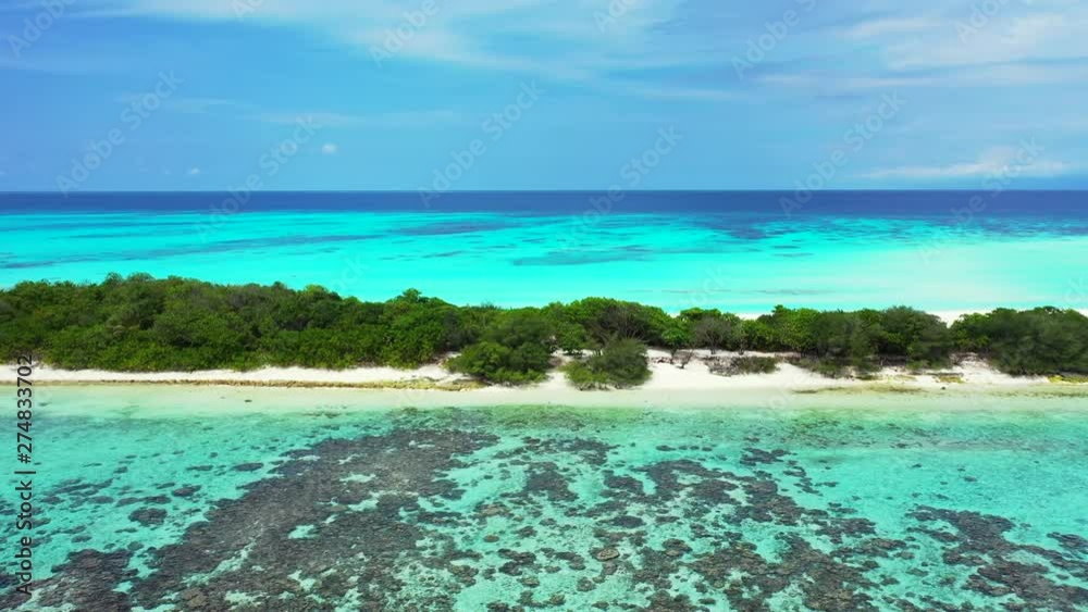 Aerial view of a long and thin island with trees on it. Under a blue sky with reefs in front of it. In Jamaica. Truck left